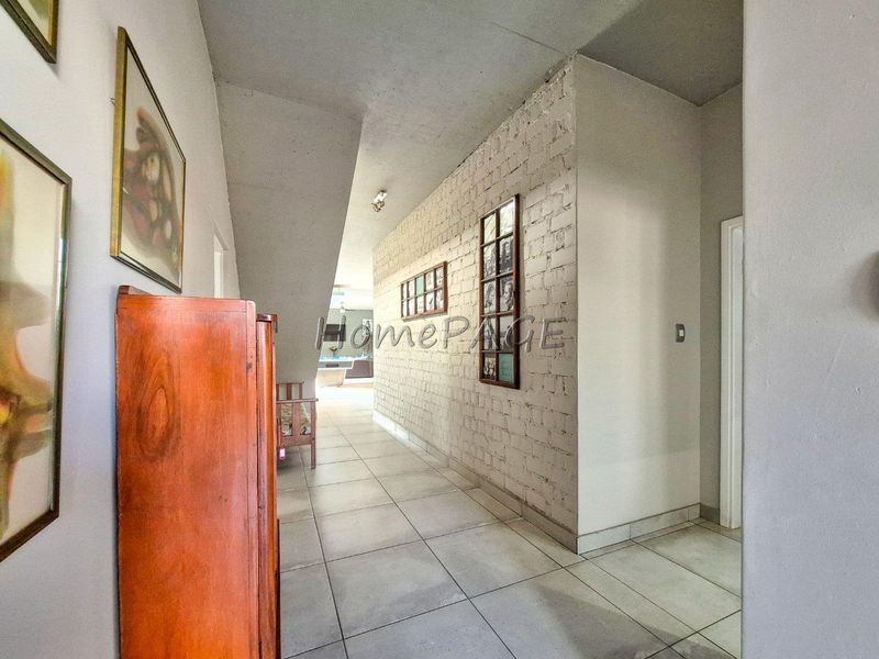 A spacious hallway featuring a textured exposed brick wall, neutral tiled flooring, and a unique sloped ceiling design leading toward the living area.