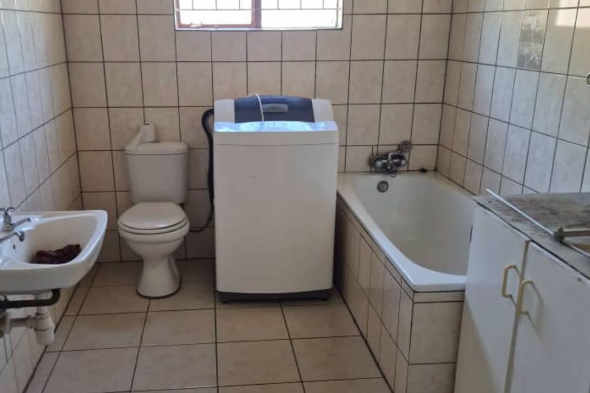 A functional bathroom featuring a built-in bathtub, wall-mounted basin, toilet, and built-in vanity cabinetry with tiled finishes throughout.