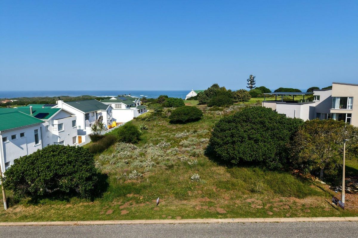 An aerial view of a vacant residential plot situated in a coastal neighborhood, offering potential for development with surrounding established homes.