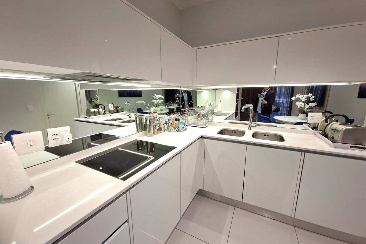 Modern kitchen featuring high-gloss white cabinetry, stone countertops, integrated induction hob, double sink, and a sleek mirrored splashback with under-cabinet lighting.