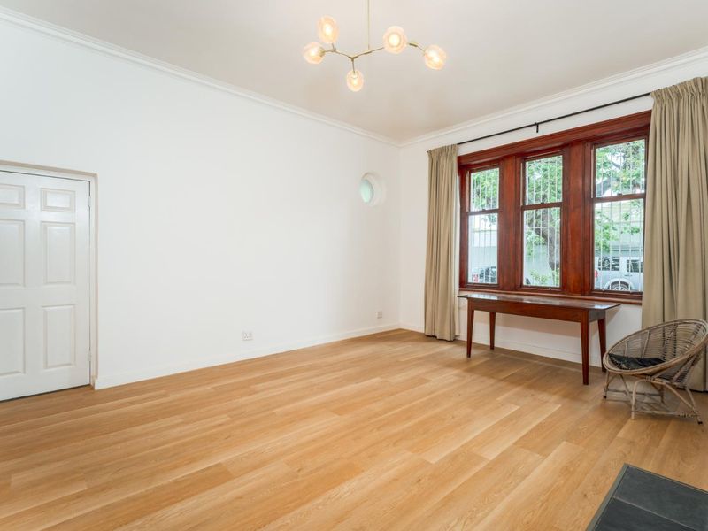 Spacious living room featuring polished hardwood flooring, large timber-framed windows with security bars, and a modern ceiling light fixture.