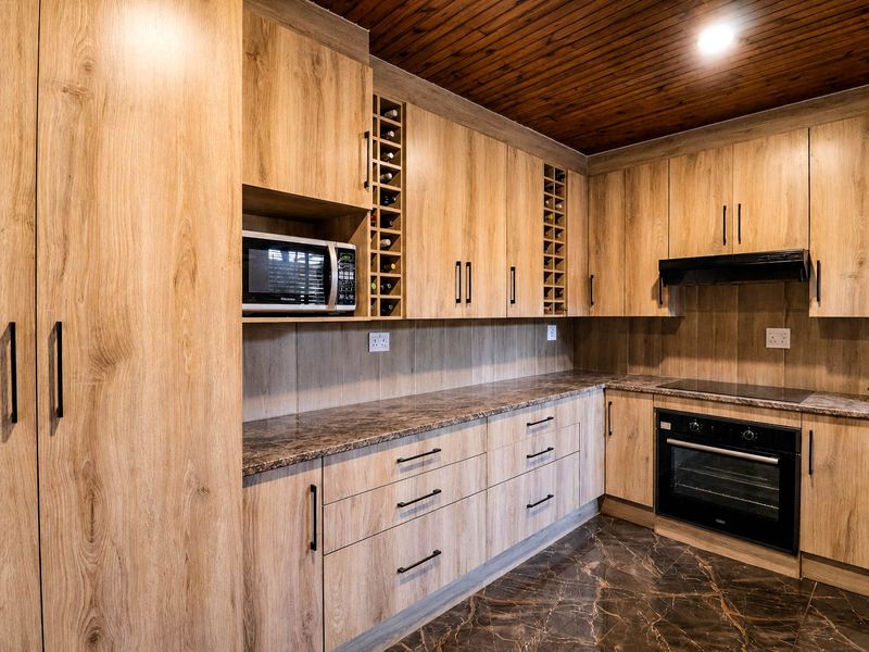 Modern kitchen featuring light wood-look cabinetry, stone-effect countertops, integrated appliances, and a distinctive timber slat ceiling.