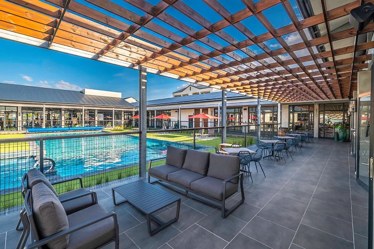 A well-maintained outdoor pool area featuring a large swimming pool, a modern timber pergola, and tiled patio space with glass balustrades.