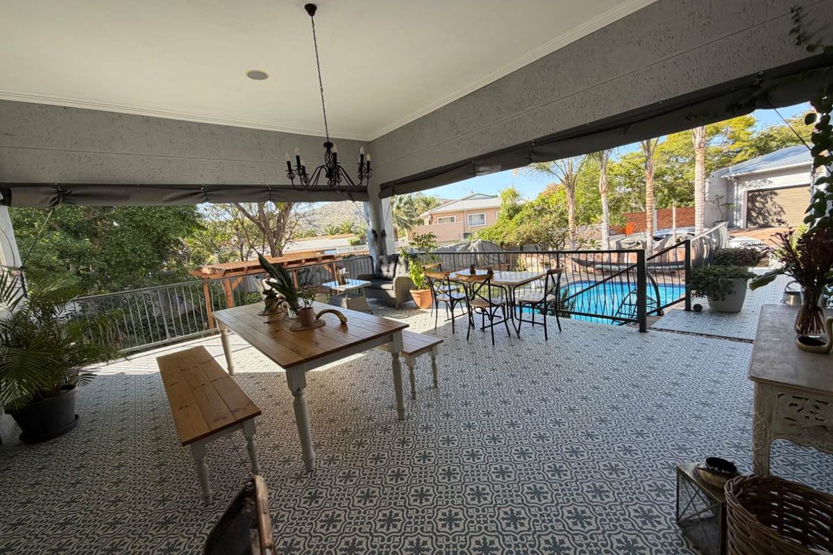 Spacious covered patio featuring decorative patterned floor tiles, wrought iron railings, and views overlooking the swimming pool and garden area.
