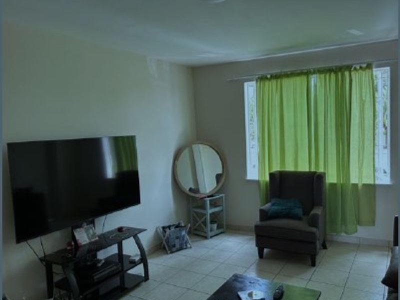 A living room area featuring tiled flooring and a large window, providing a functional space for relaxation.