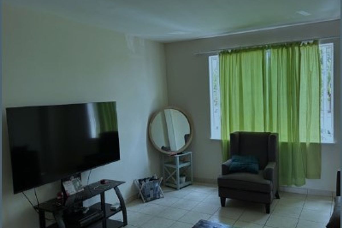 A living room area featuring tiled flooring and a large window, providing a functional space for relaxation.
