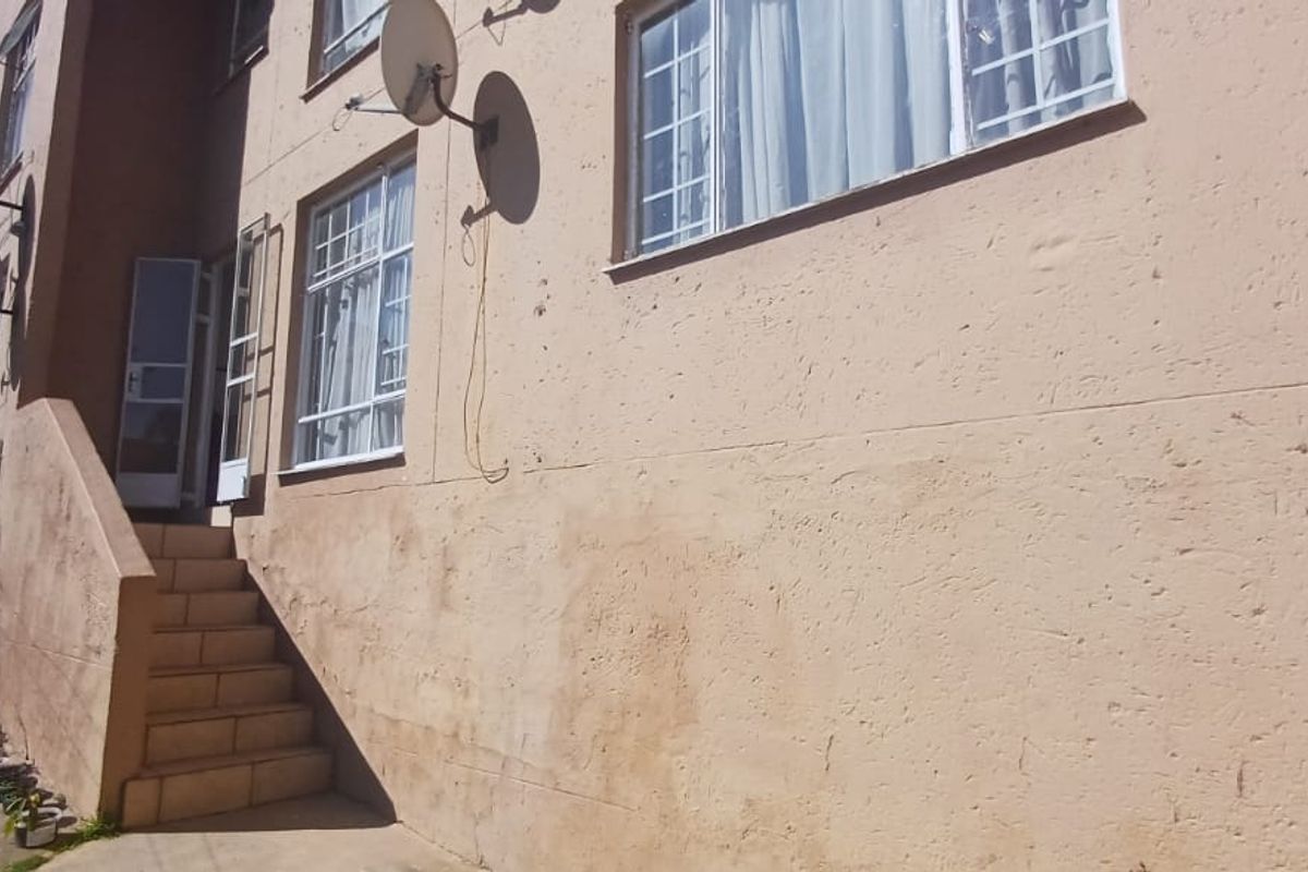 Exterior view of the apartment building featuring a concrete staircase, security gates, and multiple satellite dishes mounted on the facade.