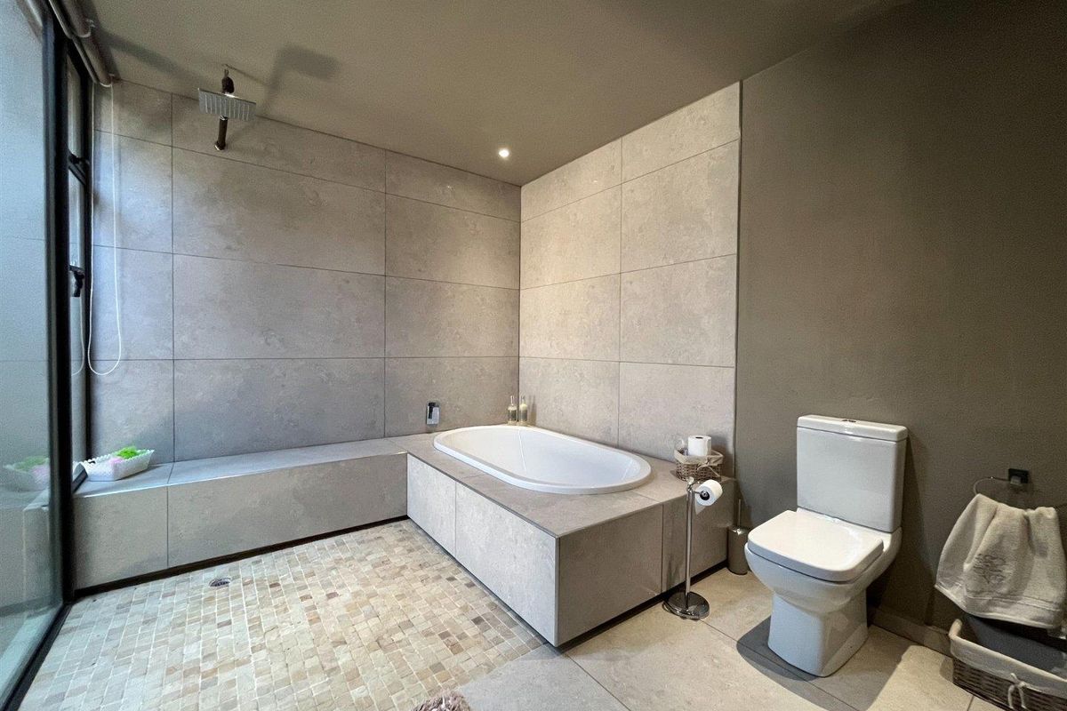 Modern bathroom featuring a built-in bathtub, walk-in shower area with mosaic floor tiling, large format wall tiles, and a contemporary toilet.