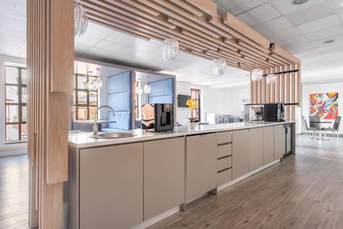 Modern office kitchenette featuring sleek cabinetry, integrated sink, and decorative timber slat ceiling detail, creating a professional and inviting break area.