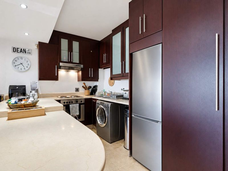 Compact kitchen featuring dark wood cabinetry, stone countertops, integrated appliances, and a built-in oven with an extractor fan.
