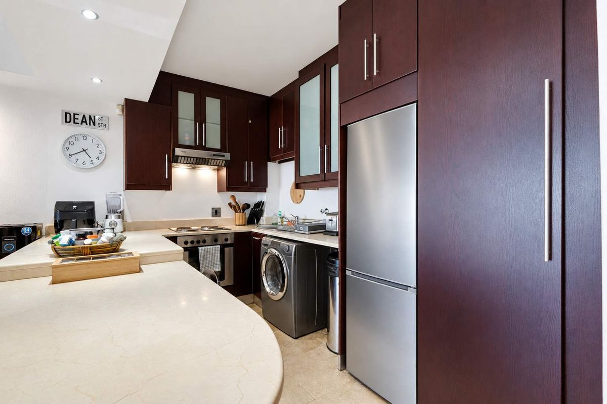 Compact kitchen featuring dark wood cabinetry, stone countertops, integrated appliances, and a built-in oven with an extractor fan.