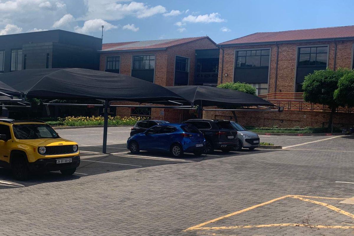 Exterior view of a commercial office complex featuring a paved parking lot with shaded carports and brick building architecture.
