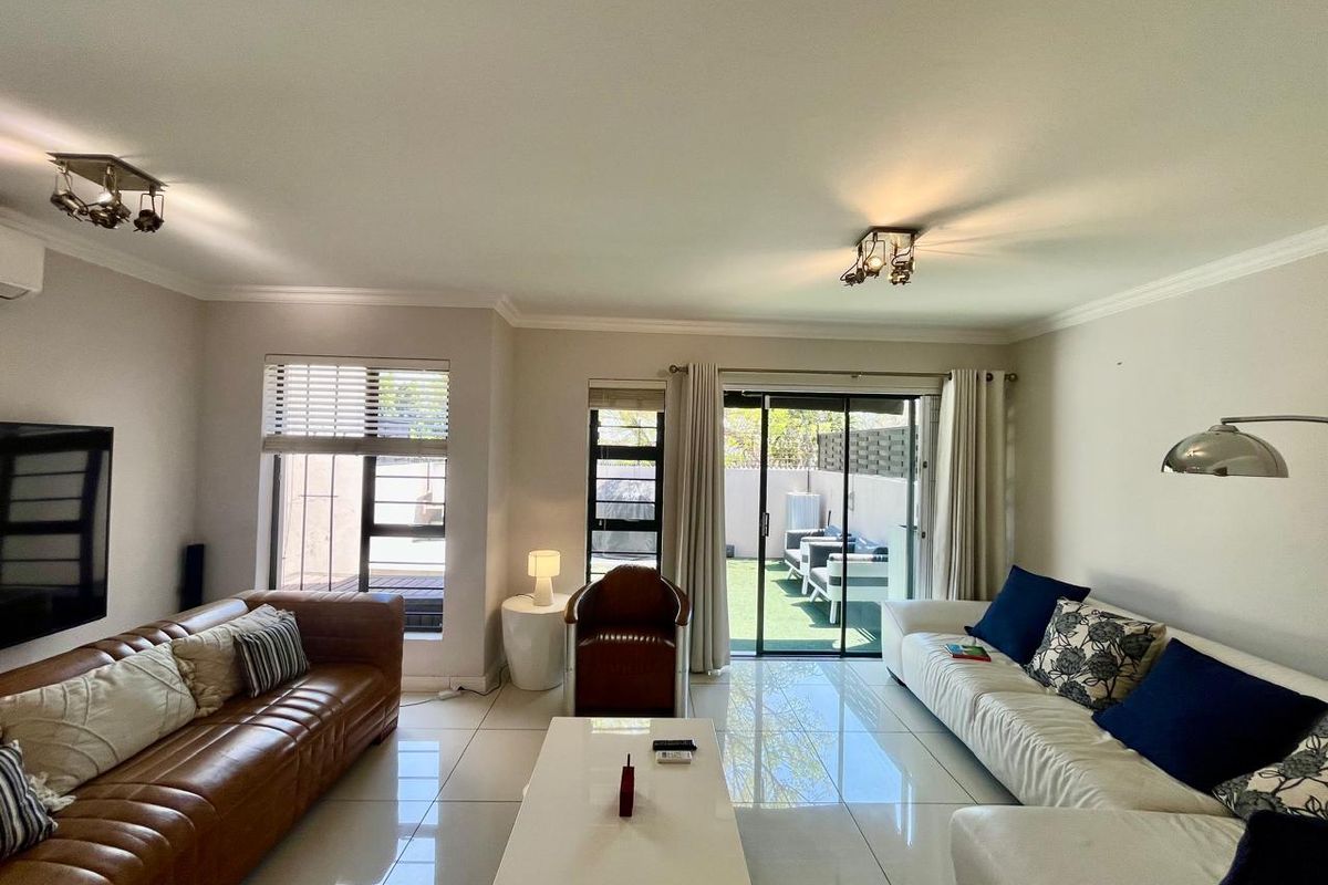 A bright and spacious living room featuring large format floor tiles, modern lighting, and sliding glass doors that provide direct access to the outdoor patio.