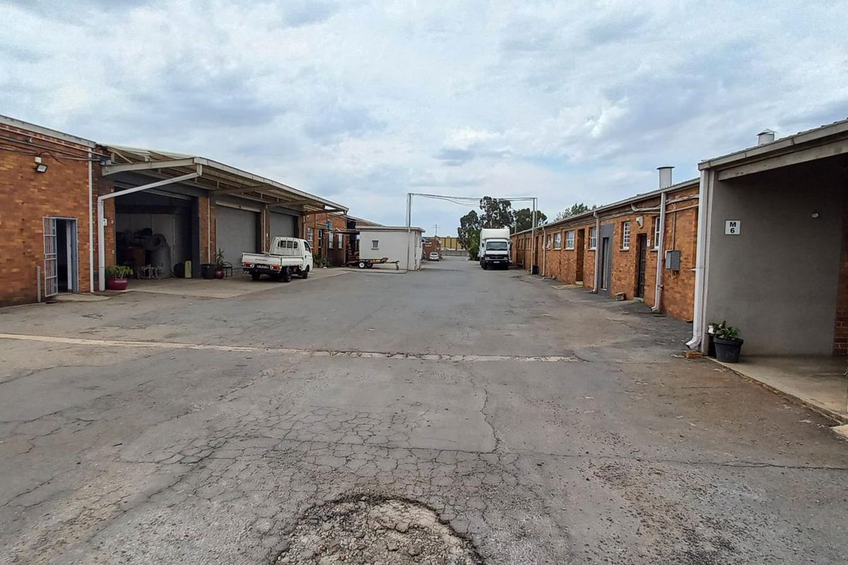 Industrial complex courtyard featuring multiple warehouse units with brick facades, roller shutter doors, and paved access driveway.