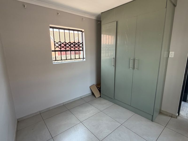 A functional bedroom featuring neutral tiled flooring, a built-in wardrobe, and a window fitted with security bars.