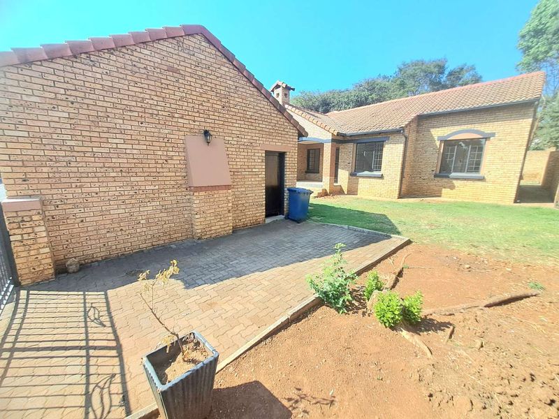 Rear view of the townhouse featuring a face brick facade, tiled roof, and a paved patio area leading onto a garden space.