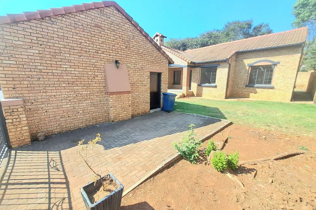 Rear view of the townhouse featuring a face brick facade, tiled roof, and a paved patio area leading onto a garden space.