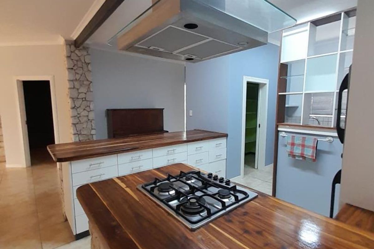 Modern kitchen featuring a central island with a built-in gas hob, stainless steel extractor fan, and natural wood countertops with stone cladding accents.