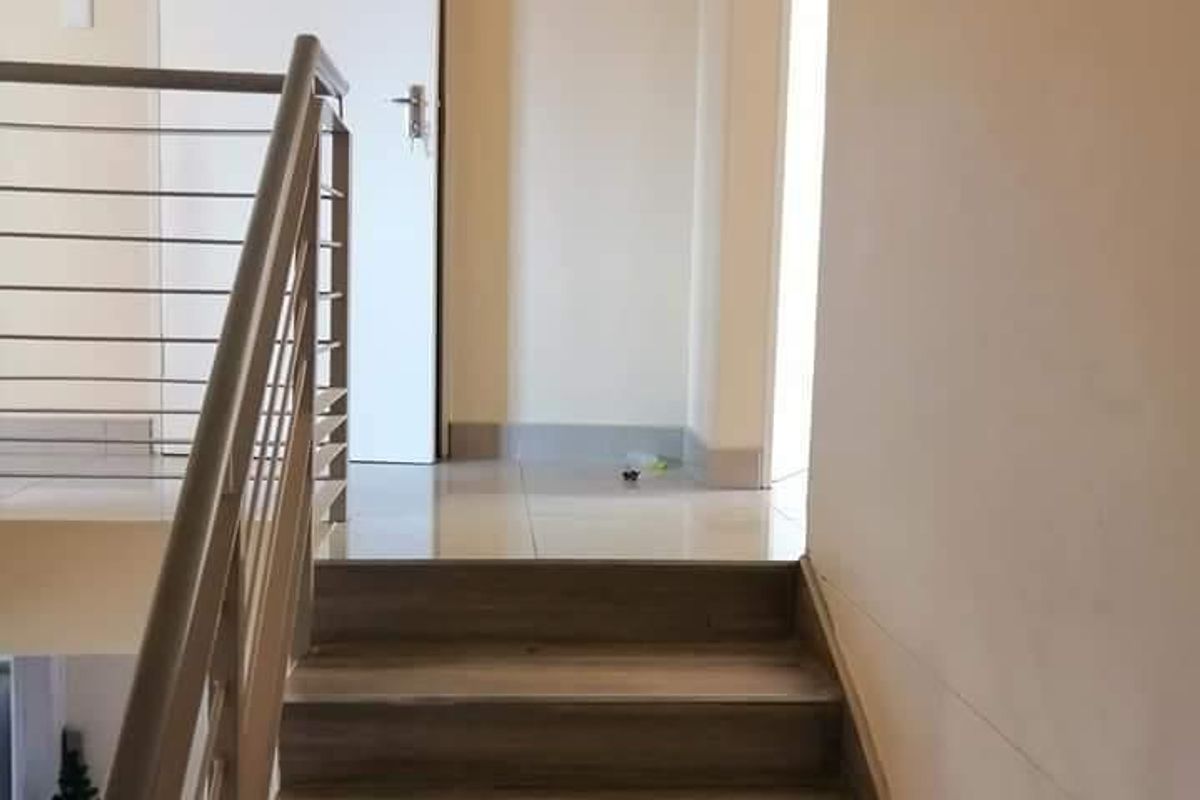 A clean, modern staircase featuring wood-look treads and a stainless steel balustrade, leading to an upper landing with tiled flooring.