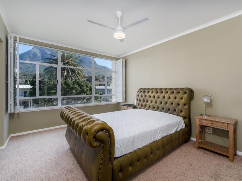 A well-lit bedroom featuring carpeted flooring, a ceiling fan, and large windows with plantation shutters offering scenic mountain views.