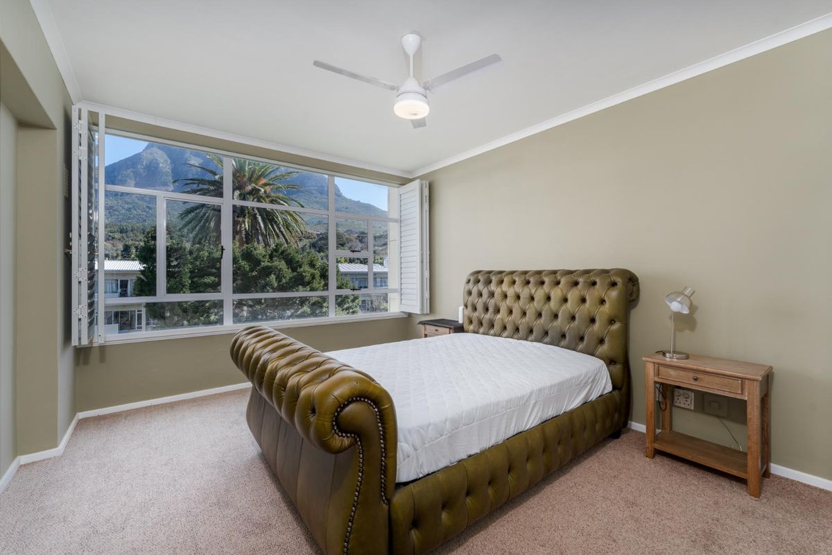 A well-lit bedroom featuring carpeted flooring, a ceiling fan, and large windows with plantation shutters offering scenic mountain views.