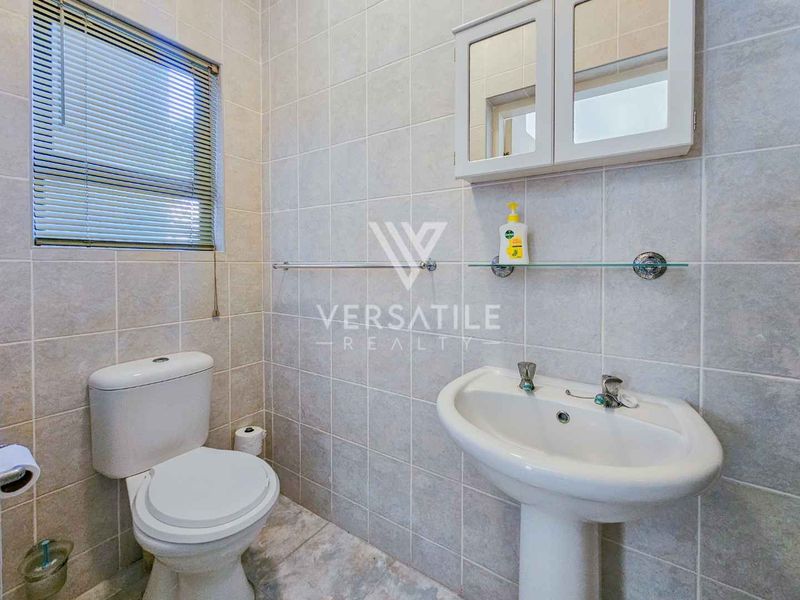 A functional bathroom featuring a pedestal sink, toilet, and wall-mounted medicine cabinet, finished with neutral wall and floor tiling.