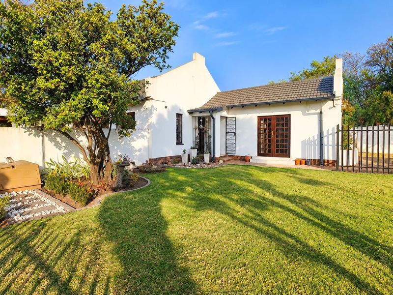 A well-maintained rear exterior view of the house featuring a manicured lawn, mature tree, and classic french doors leading to the garden.