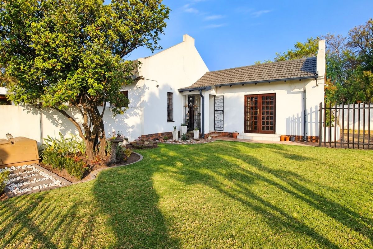 A well-maintained rear exterior view of the house featuring a manicured lawn, mature tree, and classic french doors leading to the garden.