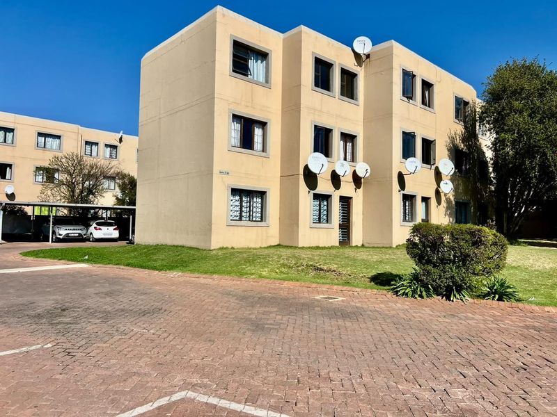 Exterior view of a multi-story apartment complex featuring a paved driveway, carport parking, and multiple satellite dish installations on the facade.