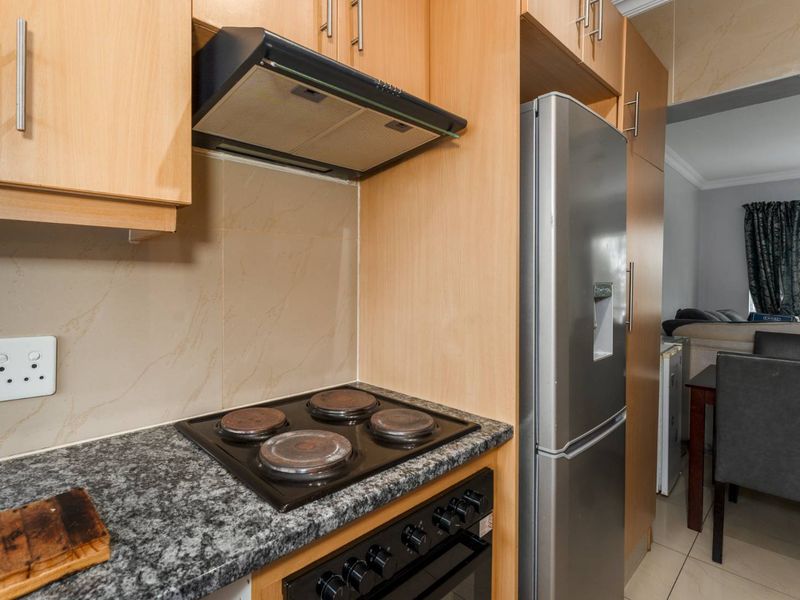 A functional kitchen featuring light wood cabinetry, granite countertops, a built-in oven with electric hob, and a tiled backsplash.