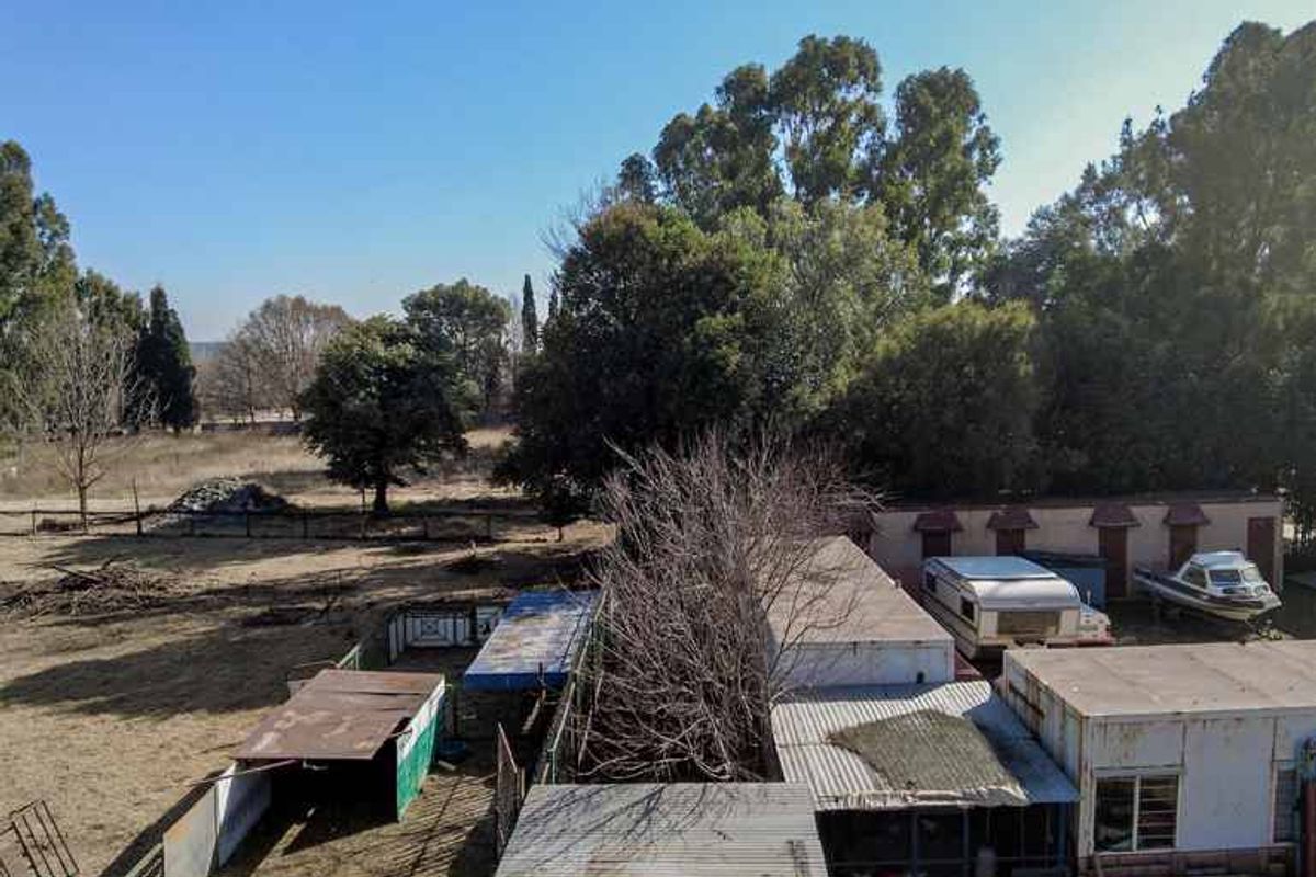 An elevated view of the rear property area featuring multiple outbuildings with corrugated metal roofing and surrounding fenced grounds.