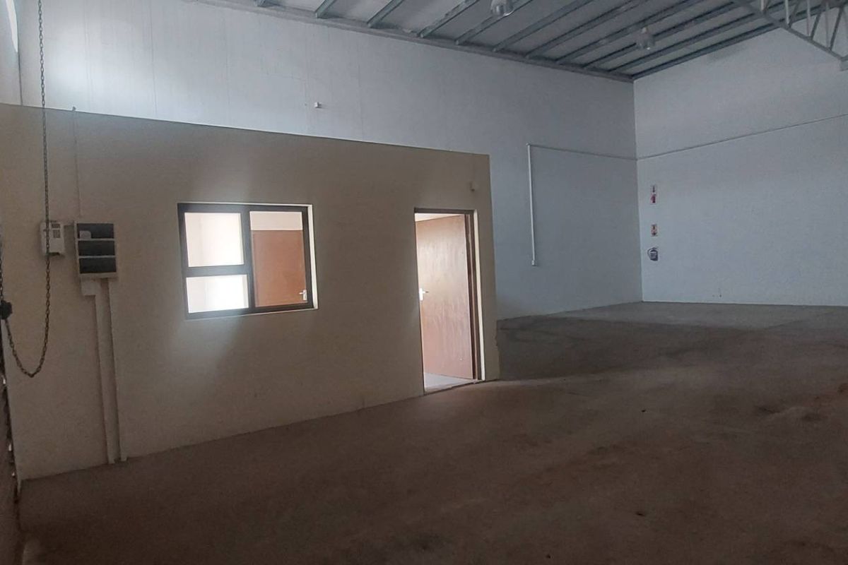 Spacious industrial warehouse unit featuring high ceilings with exposed steel trusses, a roller shutter door, and a partitioned internal office space.