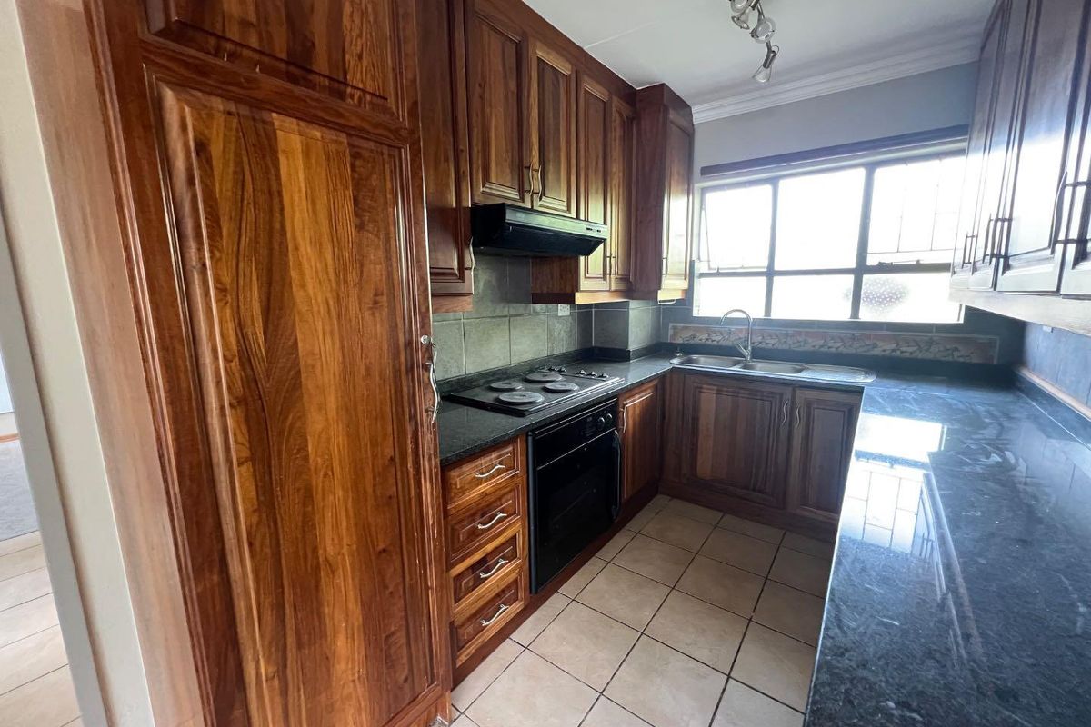 A functional kitchen featuring dark wood cabinetry, granite countertops, a built-in oven with hob, extractor fan, and tiled flooring.