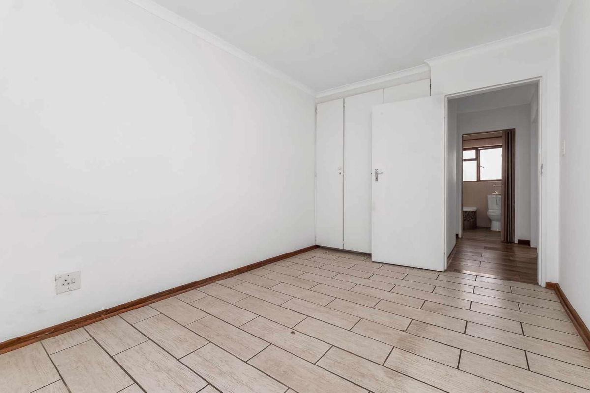An empty bedroom featuring tiled flooring, built-in cupboards, and direct access to an adjacent bathroom.