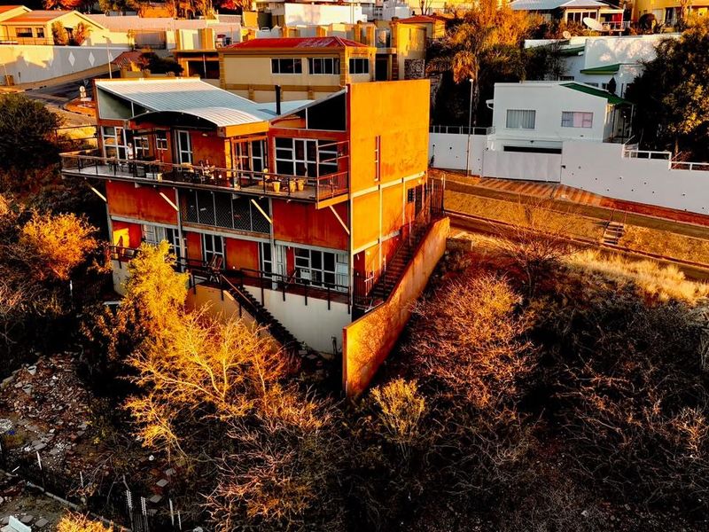 Aerial view of a multi-level residential property featuring external staircases, balconies, and a metal roof, situated in a hillside neighborhood.