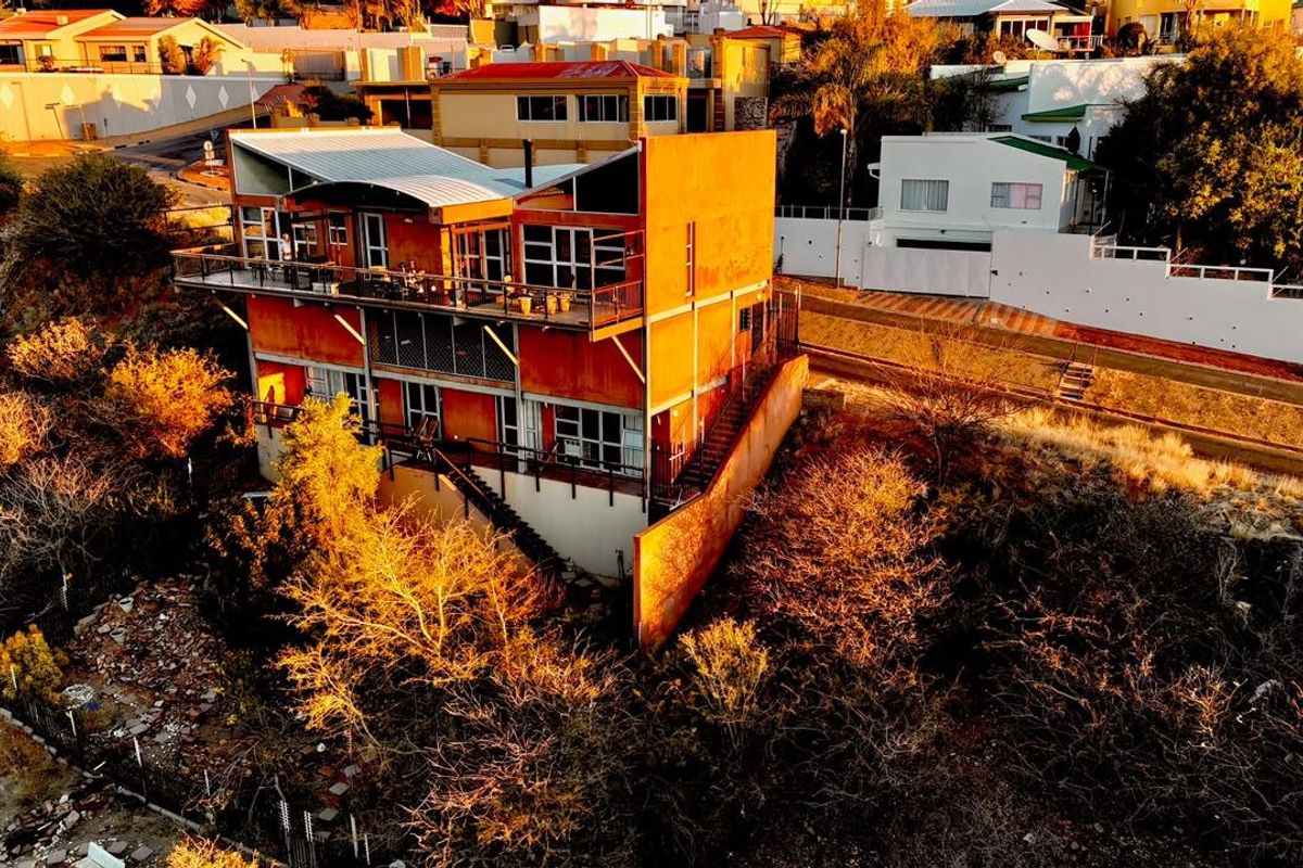 Aerial view of a multi-level residential property featuring external staircases, balconies, and a metal roof, situated in a hillside neighborhood.
