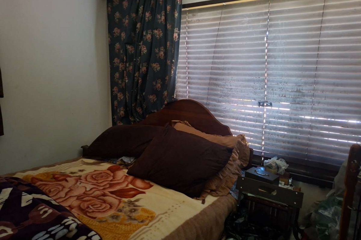 A bedroom featuring a window with venetian blinds and curtain fixtures, requiring cosmetic updates to improve the overall aesthetic and condition.