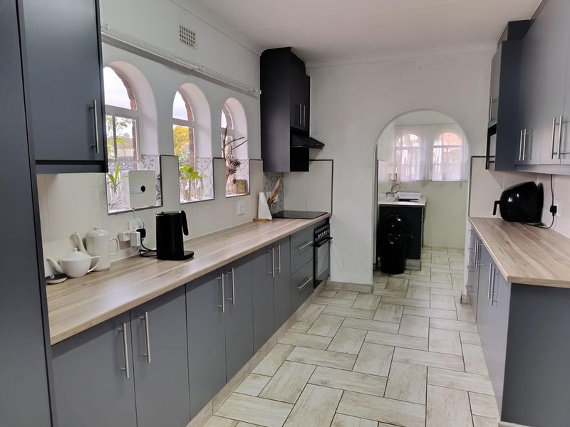 A well-maintained kitchen featuring modern grey cabinetry, wood-look laminate countertops, built-in oven and hob, and distinctive arched windows with tiled flooring.