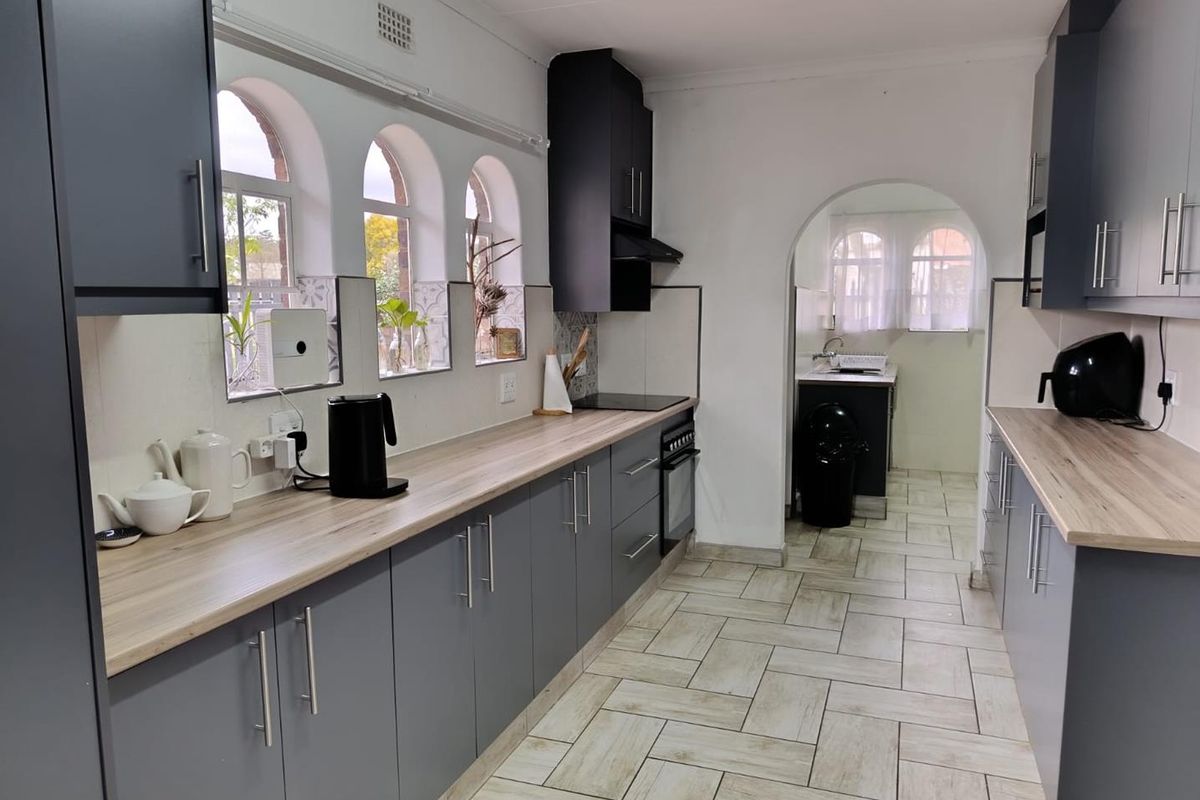 A well-maintained kitchen featuring modern grey cabinetry, wood-look laminate countertops, built-in oven and hob, and distinctive arched windows with tiled flooring.