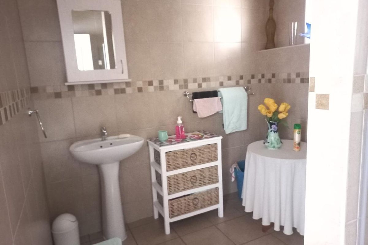 A functional bathroom featuring a pedestal sink, wall-mounted medicine cabinet, and neutral wall tiling with a decorative mosaic border.