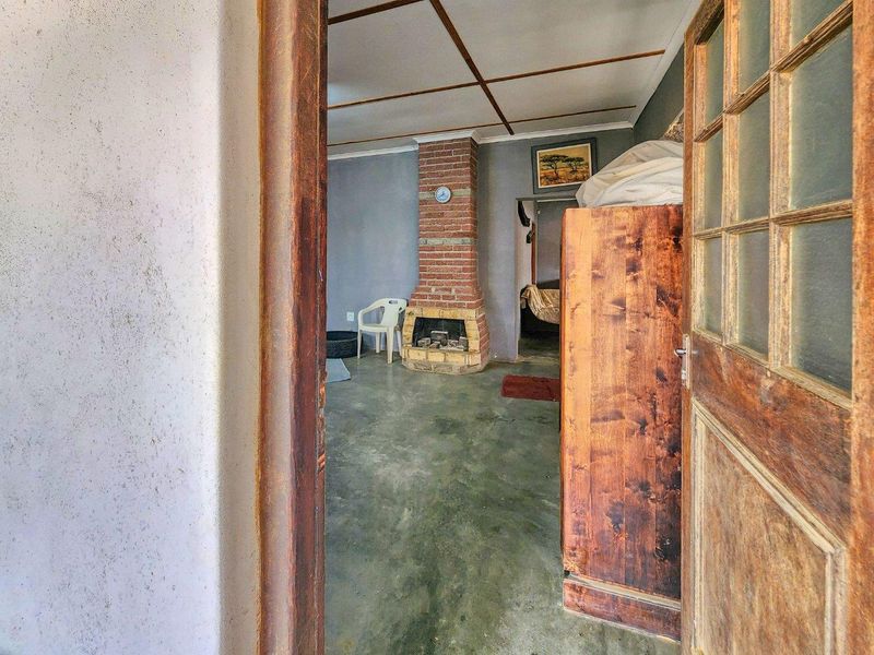 A living room featuring a brick fireplace and exposed beam ceiling, with concrete flooring and a traditional timber door frame.