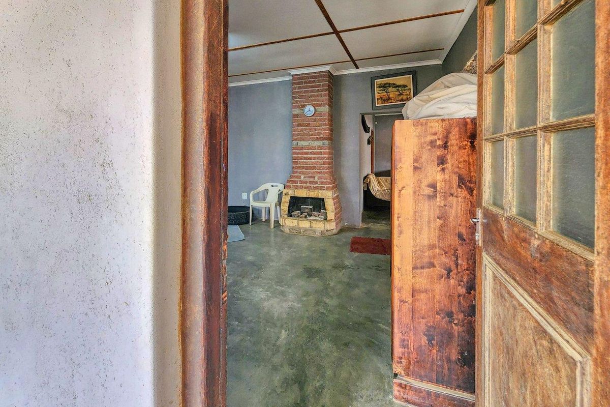 A living room featuring a brick fireplace and exposed beam ceiling, with concrete flooring and a traditional timber door frame.