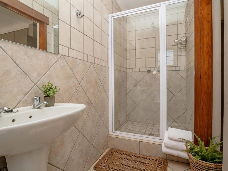 A functional bathroom featuring a pedestal basin, a tiled shower enclosure with a glass door, and neutral wall tiling.