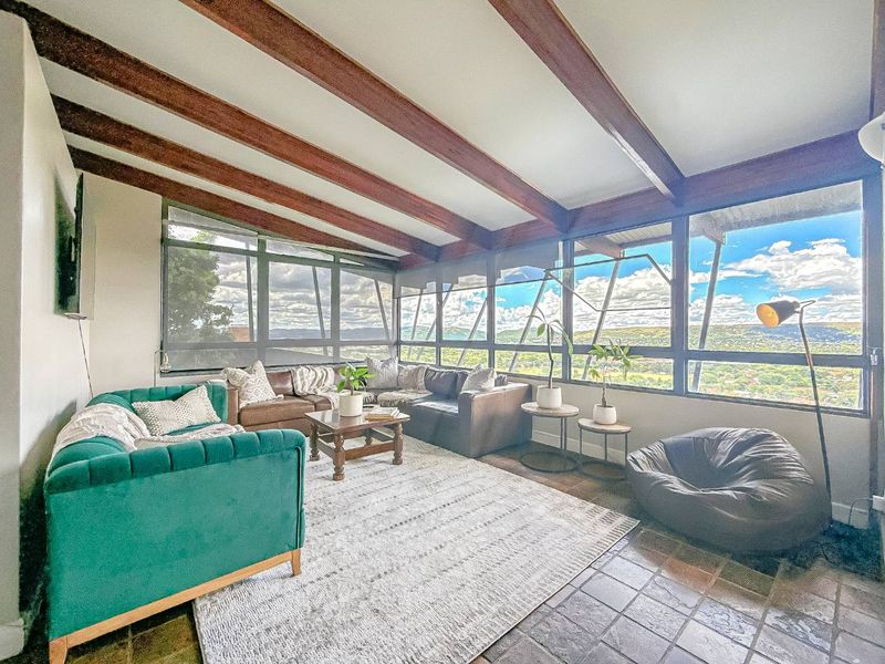 Spacious living room featuring exposed timber ceiling beams, tiled flooring, and expansive windows offering panoramic landscape views.