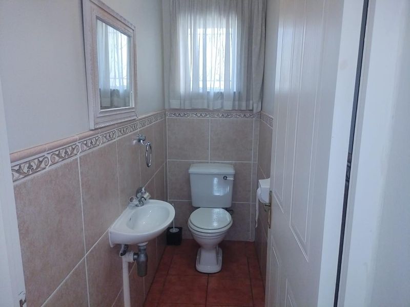 A compact bathroom featuring ceramic wall and floor tiles, a pedestal basin, and a standard toilet with a decorative border tile finish.
