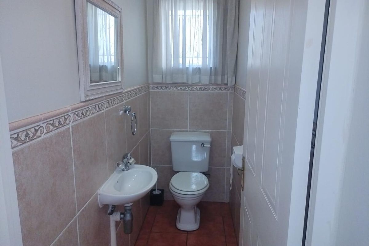 A compact bathroom featuring ceramic wall and floor tiles, a pedestal basin, and a standard toilet with a decorative border tile finish.