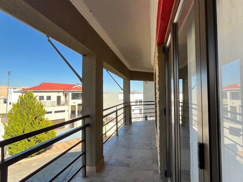 A spacious covered balcony featuring tiled flooring, metal balustrades, and large sliding glass doors, offering a clean and well-maintained outdoor living space.