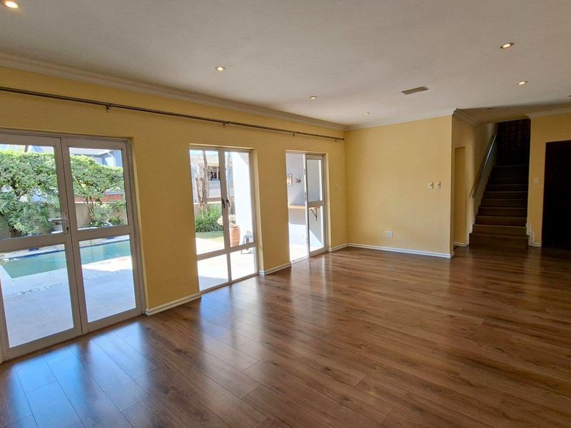 Spacious, light-filled living area featuring laminate flooring, recessed lighting, and direct access to the outdoor pool area through glass sliding doors.