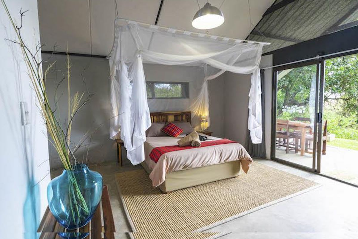 A spacious bedroom featuring a canopy bed, polished concrete flooring, and large sliding glass doors that open onto a private patio area.