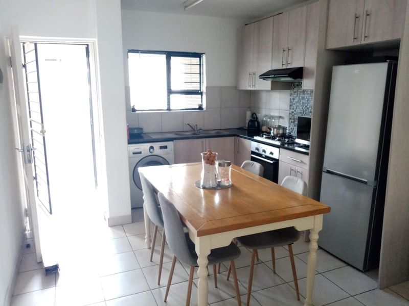 Open plan kitchen and dining area featuring built-in cabinetry, tiled flooring, and direct access to an exterior door with a security gate.